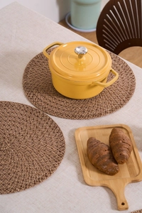 Detail of round woven jute placemat with yellow enamel cast iron pot on dining table