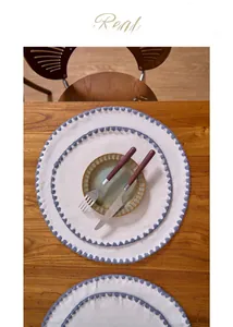 Close-up of cream round placemats with blue scalloped embroidery on wood table