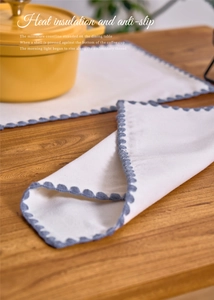 Detail of white cotton table mat with blue scalloped embroidery and heat insulation