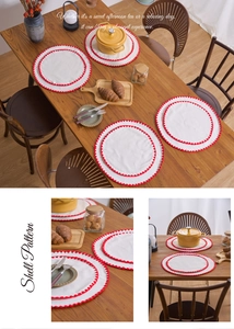 Detail of round cotton placemat with decorative red shell pattern stitching on table