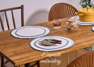 Detailed view of cream placemats with blue embroidered scallop edges and cotton texture