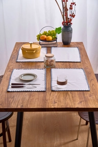Detail showing white rectangular placemats with deep blue pom-pom fringe edges on wood table
