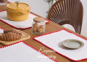 Close-up of white cotton linen placemat with delicate red wavy embroidery and rustic design