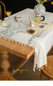 Detailed view of beige tablecloth with green vine leaf prints and fringe tassels on wood table