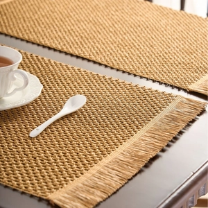 Natural woven placemats with tassel fringe in light brown on a dark wooden dining table