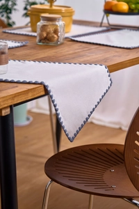 Detail of white cotton table runner with blue pompom trim draping over a wooden table edge