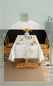 Detail of embroidered green leaf pattern and beige tassel edges on cotton linen tablecloth