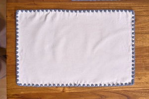 Close-up of cream rectangular placemat with blue scalloped edges on wooden table