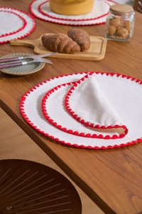 Detail of round cotton linen placemats with red scalloped edges in various sizes