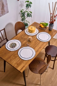 Detailed view of round cream placemats with blue embroidered edges on a wooden table