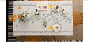 Close-up of elegant green vine embroidery on a cream cotton linen textured tablecloth
