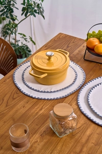 Detailed view of an embroidered white round place mat under a yellow cast iron pot