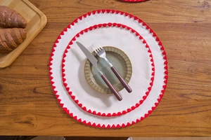 Close-up of round beige linen placemats with red scalloped edges on a wooden table