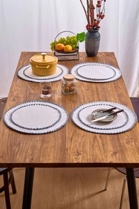 Close-up of beige round placemats with blue embroidered pom-pom edge on a wooden table
