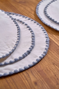 Detail of round white cotton placemats with blue scalloped embroidery on wood table