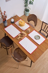 Close-up of four cream cotton linen placemats with red scalloped embroidered edges