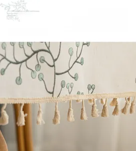 Detailed embroidery of green leaves and cream tassels on a linen fabric tablecloth