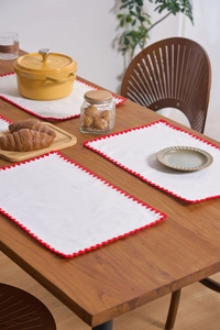 Close-up of white cotton linen placemat with red scalloped crochet edge on wooden table