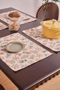 Close-up of four thick linen placemats with festive gingerbread and tree patterns