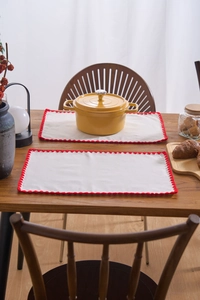 Detail of cream linen placemats with red scalloped edges on a rustic wooden table