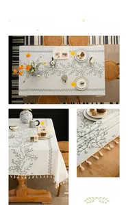 Close-up of embroidered green vines and berries with cream tassels on linen tablecloth