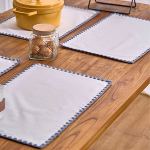 Set of 4 white cotton linen placemats with blue scalloped edges on a wooden table