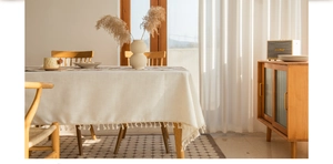 Detailed close-up of light beige tablecloth with textured fabric and fringe tassel edges