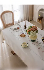 Detail of cream floral embroidery and fringe tassels on a French linen style tablecloth