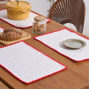 White cotton linen placemats with red scalloped edges on a rustic wooden dining table
