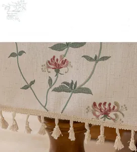 Macro shot of French cream floral embroidery and handcrafted tassels on linen tablecloth