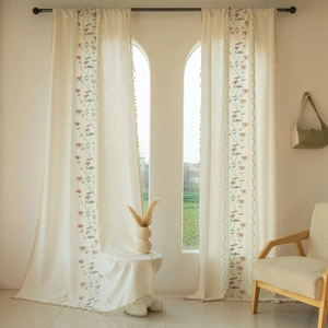 Detail of beige curtain with delicate floral embroidery and decorative tassel edges