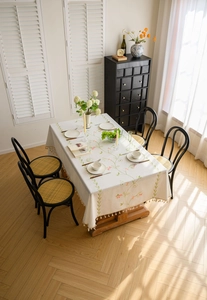 Detail of floral embroidery and tassels on creamy white cotton linen tablecloth