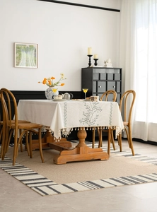 Close-up of beige linen tablecloth with green vine embroidery and tassel edges