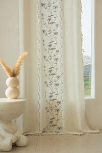 Detailed close-up of beige linen curtains with blue flower embroidery and fringe edges