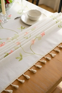 Close-up of floral embroidery and beige tassel fringe on cotton linen tablecloth