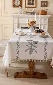 Détail de broderies florales grises et pompons sur nappe rectangulaire en lin beige