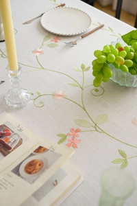 Detail of floral embroidery on off-white linen tablecloth with rustic fringe and leaves