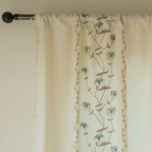 Close-up of beige fabric curtain with blue flower embroidery and side tassel detail