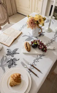 Détail de motifs floraux gris brodés sur nappe en lin beige avec des glands