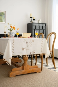 Detailed embroidery with plant patterns and handmade tassels on beige linen tablecloth