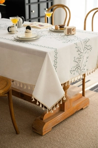 Close-up of beige linen tablecloth with green leaf embroidery and elegant tassel edges