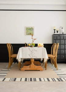 Detailed close-up of floral embroidery and tassels on an off-white cotton-linen tablecloth