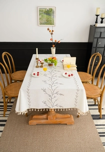 Detail of floral embroidery and fringe tassels on a white linen rectangular tablecloth
