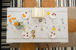 Detailed overhead view of beige rectangle tablecloth with vintage floral embroidery and tassels