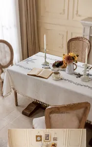 Détail de fleurs et papillons gris brodés sur nappe en lin beige avec bordures à glands