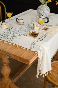 Detail of embroidered green vine leaves and beige tassels on a cotton linen tablecloth
