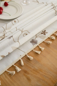Detail of floral embroidery on linen-textured tablecloth with elegant beige fringe
