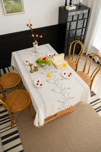 Detail of white rectangular tablecloth with lilac embroidery and fringe edge on wood table