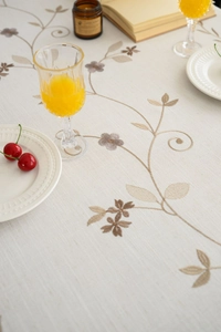 Close-up of elegant floral embroidery and tassel detail on linen tablecloth fabric