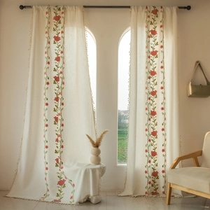 Close-up of beige embroidered curtains featuring red floral patterns and elegant tassel trim